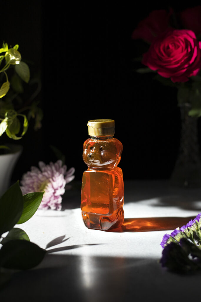 a plastic bear honey container next to flowers.