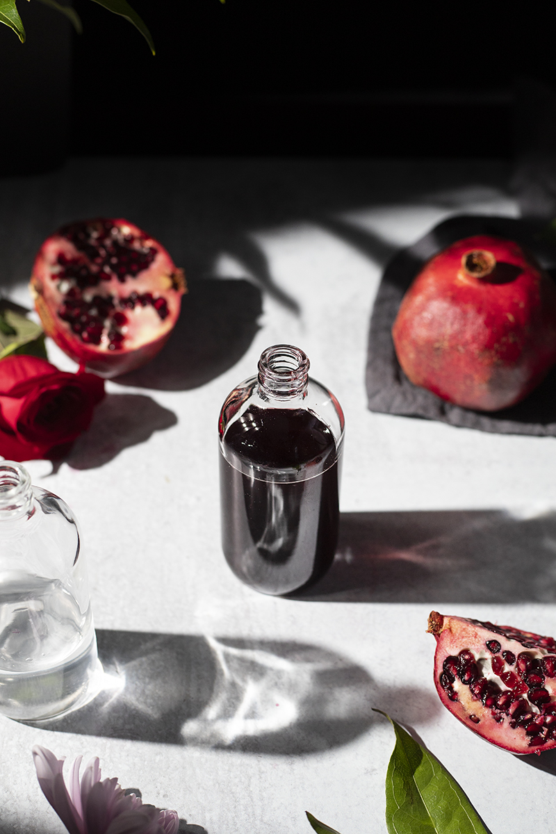 a small apothecary bottle with dark red liquid surrounded by pomegranates