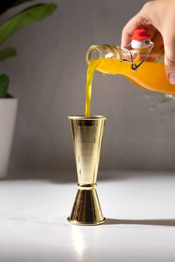 close up of pouring turmeric syrup into a gold bar jigger.