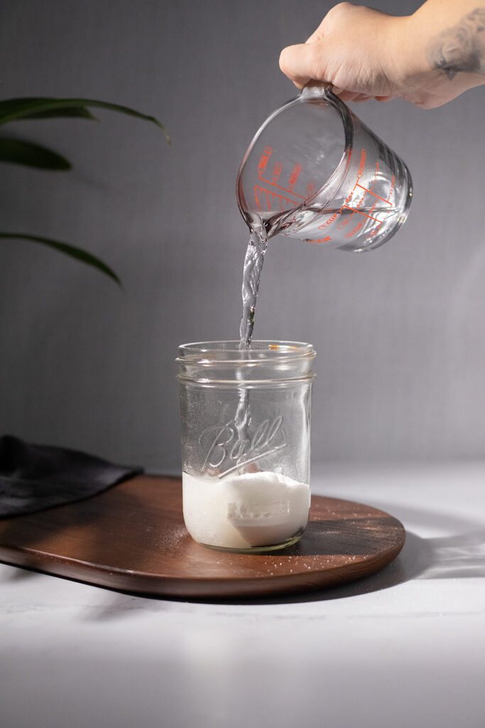 pouring water from a measuring cup into a glass jar.