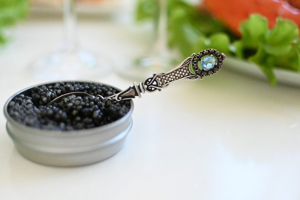 A jar of caviar with an elegant teaspoon on top of a white table