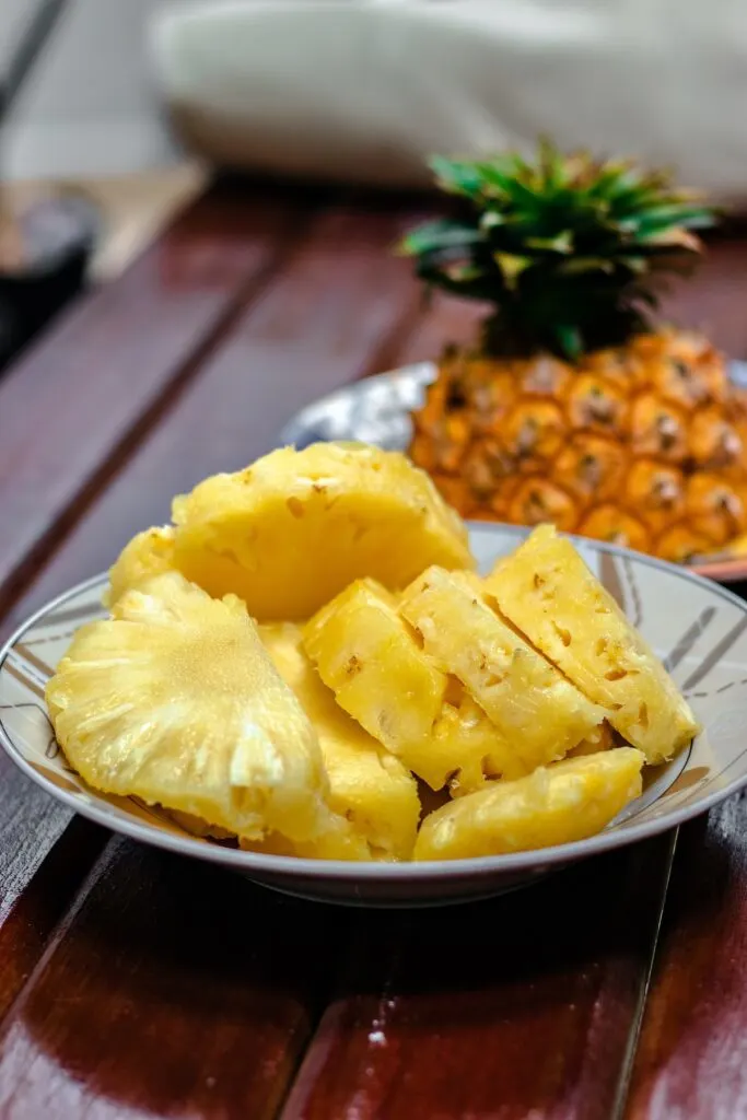 A plate of sliced pineapple next to half of unsliced pineapple