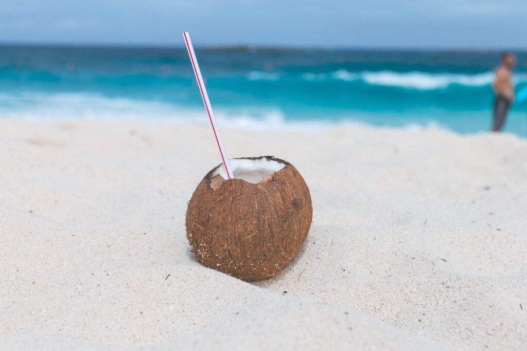 Brown coconut with plastic straw on the sand
