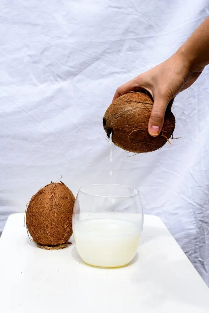 A person pouring coconut milk in a clear glass
