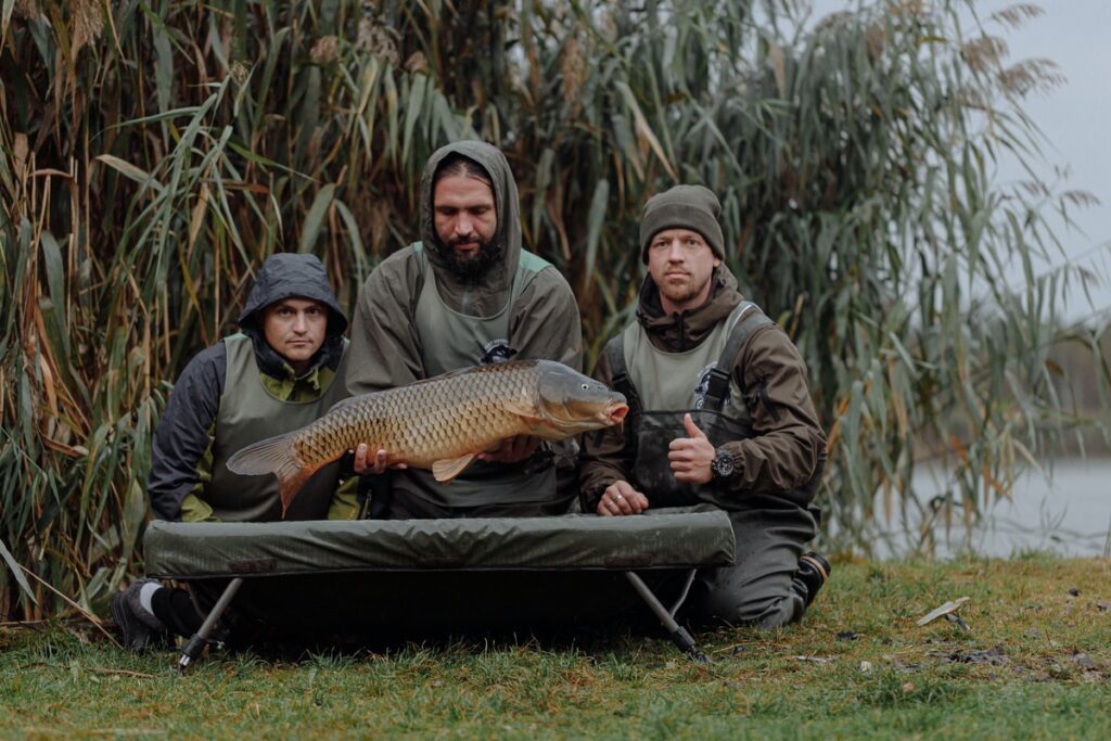 Three men sitting on the grass with the one in the middle holding a big carp